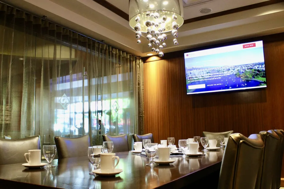 The 65-inch TV in the Cambie Room at Chateau Granville, beside sheer-curtained windows onto Granville Street